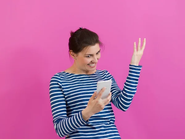 Ein überraschtes Mädchen blickt auf ihr Handy, als sie vor einem rosafarbenen Hintergrund steht — Stockfoto