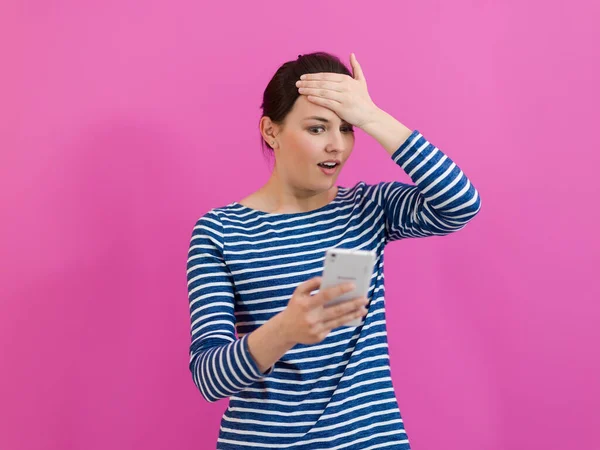 É apontado-enfrentou menina olha para seu telefone celular como ela fica na frente de um fundo rosa — Fotografia de Stock