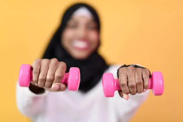 Afro musulmana mujer promueve una vida saludable, sosteniendo mancuernas en sus manos — Foto de Stock