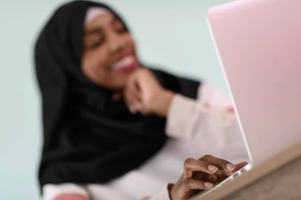 Afro muzułmanka ubrana w hidżab siedzi uśmiechnięta w swoim biurze i używa laptopa — Zdjęcie stockowe