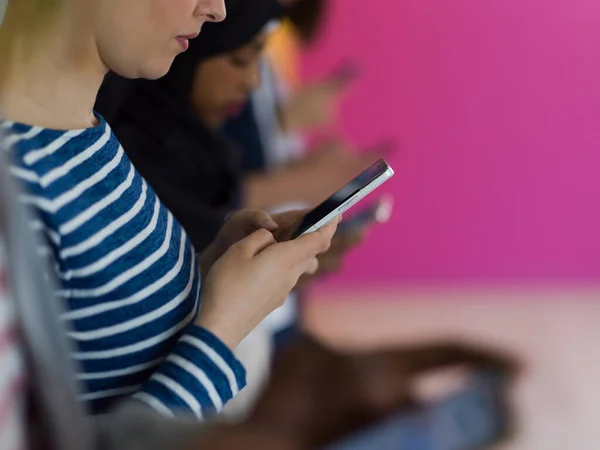 Różnorodne nastolatki używają urządzeń mobilnych podczas pozowania do zdjęcia studyjnego przed różowym tłem — Zdjęcie stockowe