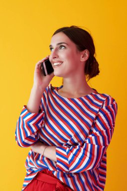 Sarı arka planda dikilirken telefonla konuşan genç kızın portresi. Modern moda ve teknoloji kavramını temsil eden kadın model.