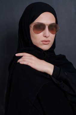 Geleneksel giysiler içinde genç Müslüman iş kadını ya da abaya ve siyah karatahtanın önünde poz veren güneş gözlüğü.