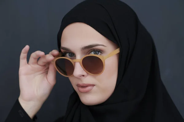 Young muslim in traditional clothes or abaya and sunglasses posing in front of black chalkboard — Stock Photo, Image