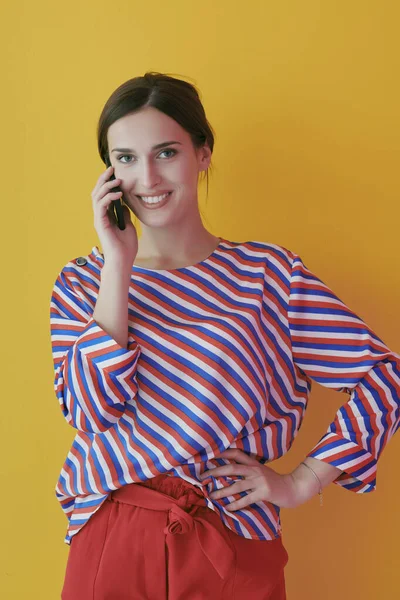 Retrato de una joven hablando por teléfono mientras está de pie frente al fondo amarillo —  Fotos de Stock