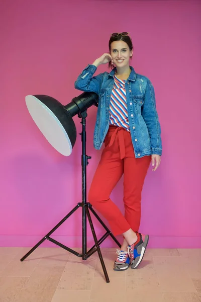 Young woman leaning against studio flashlight over a pink background — Stock Photo, Image