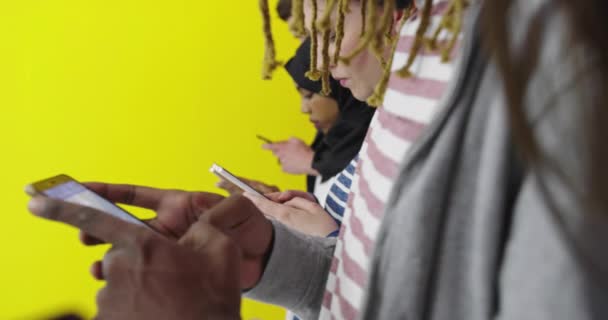 Comunicación global. Los estudiantes que envían mensajes de texto en sus teléfonos inteligentes, apoyándose en la pared de color amarillo fortuna — Vídeos de Stock