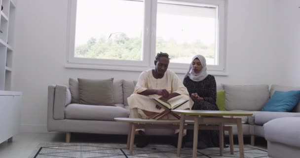 Africano casal muçulmano em casa no Ramadã leitura Alcorão azevinho Islã livro no apartamento moderno no sofá — Vídeo de Stock