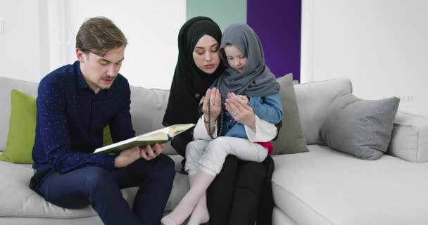 Traditionella muslimska familj föräldrar med barn som läser Koranen och ber tillsammans på soffan innan iftar middag under en Ramadan fest hemma — Stockvideo