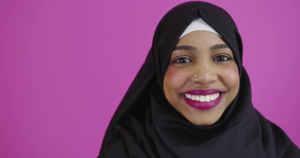 Mujer musulmana positiva usando hiyab musulmán sobre fondo colorido — Vídeos de Stock