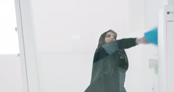 Wanita dengan jilbab celaning permukaan kaca dalam aprtment modern. — Stok Video