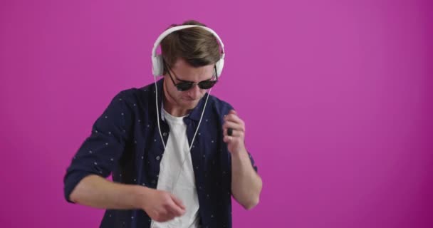 Hombre bailando y sonriendo sobre el fondo de color mientras escucha música — Vídeos de Stock