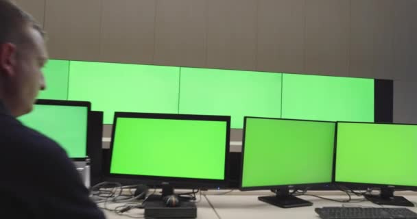 Специалист по системной безопасности работает в центре системного управления. Комната заполнена зелеными экранами, цветным экраном и системой безопасности — стоковое видео