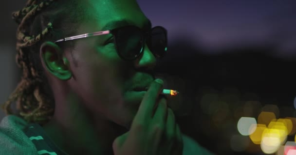 Afro americano uomo avendo partito bere e fumare con città luci in background con neon luci — Video Stock