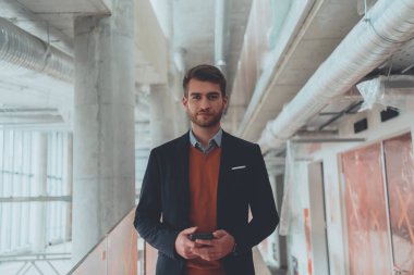 Modern bir ofis binasının şantiyesini denetlerken akıllı telefon kullanan işadamı mimar.