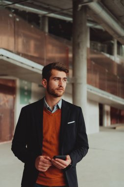 Modern bir ofis binasının şantiyesini denetlerken akıllı telefon kullanan işadamı mimar.