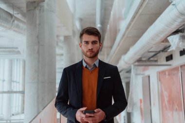 Modern bir ofis binasının şantiyesini denetlerken akıllı telefon kullanan işadamı mimar.