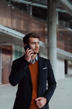 Modern bir ofis binasının şantiyesini denetlerken akıllı telefon kullanan işadamı mimar.