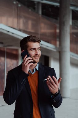 Modern bir ofis binasının şantiyesini denetlerken akıllı telefon kullanan işadamı mimar.
