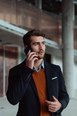 Modern bir ofis binasının şantiyesini denetlerken akıllı telefon kullanan işadamı mimar.