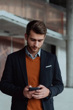 Modern bir ofis binasının şantiyesini denetlerken akıllı telefon kullanan işadamı mimar.