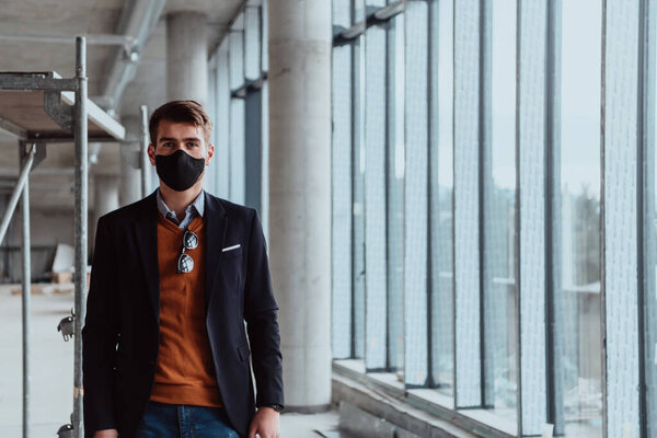 A successful entrepreneur in a suit oversees the construction of the project while wearing a mask against root virus protection