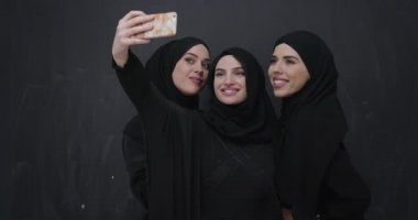 Moda kıyafetleri içinde, cep telefonu kullanan ve selfie çeken bir grup güzel Müslüman kadın.