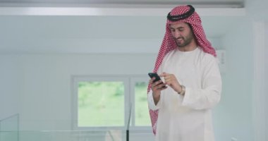 Arap işadamı evde akıllı telefon kullanırken geleneksel kıyafetler giyiyor.