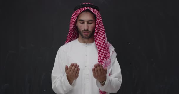 Człowiek w tradycyjnym ubraniu przed czarną tablicą modli się z otwartymi rękami — Wideo stockowe