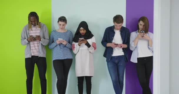 Comunicazione globale. Gli studenti che scrivono sui loro smartphone, appoggiati sulla parete a colori — Video Stock