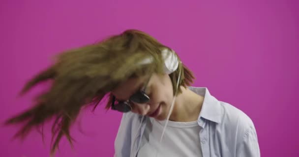 Wanita lucu memakai headphone mendengarkan musik dan menari di atas backgorund warna — Stok Video