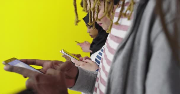 Globalna komunikacja. Studenci smsują na swoich smartfonach, opierając się na kolorowych ścianach — Wideo stockowe