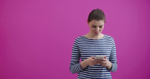 Fata tastarea și citirea mesajului text pe noul ei telefon mobil modern pe un fundal roz — Videoclip de stoc