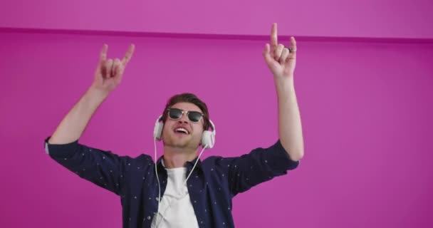 Человек танцует и улыбается на цветном фоне, слушая музыку — стоковое видео