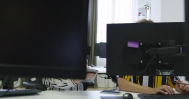 Başlangıç ofisinde iki genç iş arkadaşı bilgisayar kullanıyor ve birlikte konuşuyorlar.