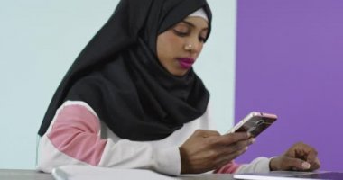 Başörtüsü takmış güzel ve mutlu bir kadın evde bir ofiste dizüstü bilgisayarla cep telefonu kullanıyor.. 