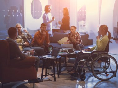 Tekerlekli sandalyedeki engelli iş kadını çeşitli iş ekibiyle buluşup modern açık alan ofis alanındaki fikirler ve planlar hakkında beyin fırtınası yapıyor. Yüksek kalite fotoğraf