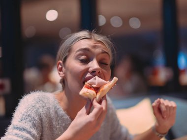 Genç kadın gece geç saatlerde modern ofiste çalışırken teslimat servisinden pizza yiyor. 