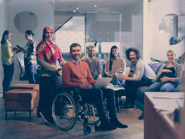 Disabled businessman in a wheelchair at work in modern open space coworking office with team