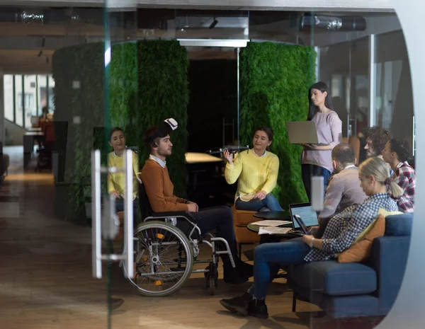 Behinderter Geschäftsmann im Rollstuhl bei der Arbeit in modernem Coworking-Büro mit Team unter Einsatz der Virtual-Reality-Brille Drohnen-Assistenzsimulation — Stockfoto