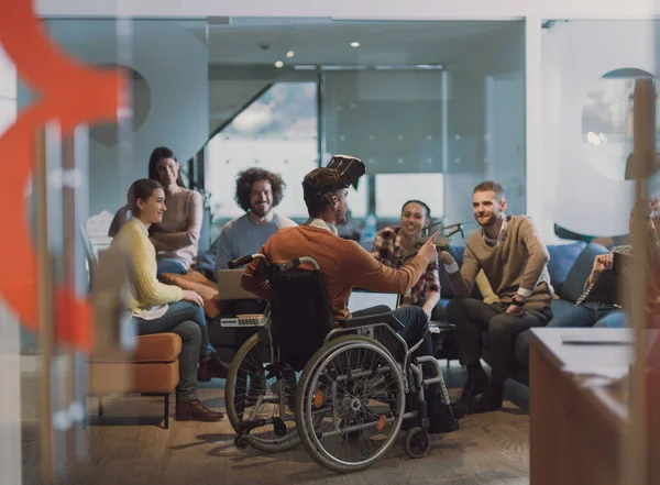 장애가 있는 사업가가 휠체어를 타고 일하고 있는 현대의 오픈 스페이스 동료 사무실에서 일하고 있습니다. 팀 과 함께 가상 현실의 구글링 드론 보조 시뮬레이션을 사용하고 있습니다. — 스톡 사진