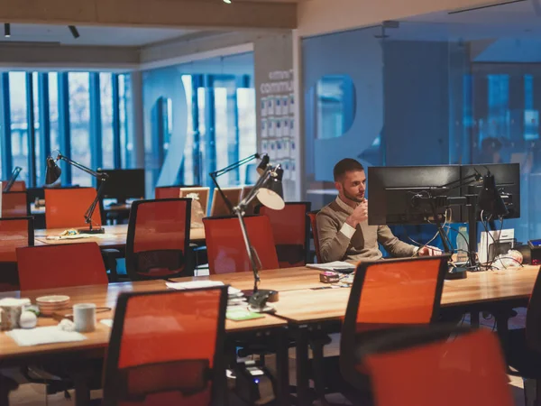 Geschäftsmann, der spätabends allein am Schreibtisch im Büro Überstunden macht — Stockfoto