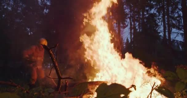 Bombero con equipo de seguridad y hacha extinguiendo fuego en el bosque por la noche — Vídeos de Stock
