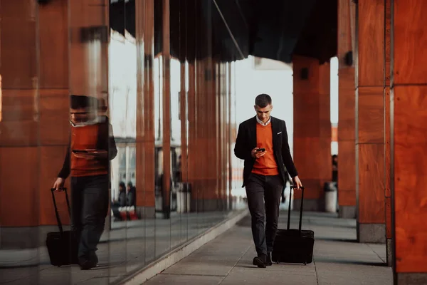 Vado al terminal dell'aeroporto. Viaggiatore d'affari fiducioso che cammina per le strade della città e tira la valigia bevendo caffè e parlando sullo smartphone — Foto Stock