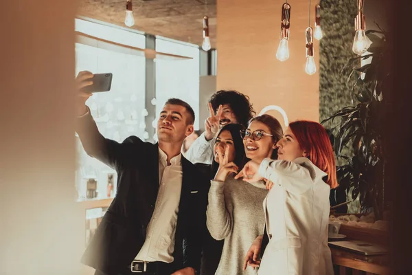 Grupo de colegas alegres tomando selfie y gestos mientras están de pie en la oficina moderna. —  Fotos de Stock