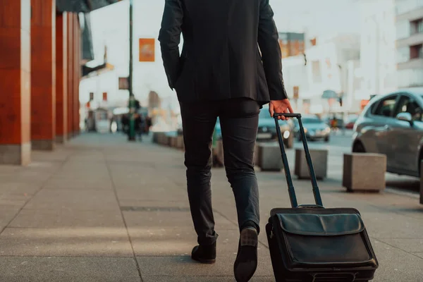 Jadę na lotnisko. Pewny siebie biznesmen podróżujący ulicami miasta, ciągnący walizkę, pijący kawę i mówiący na smartfonie — Zdjęcie stockowe