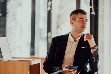 Kafeteryada dizüstü bilgisayarı ve akıllı telefonu olan mutlu bir iş adamı.