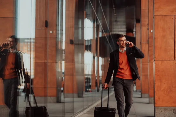 Megyek a reptérre. Magabiztos üzletember utazó sétál a város utcáin, húzza a bőröndjét kávézás és beszél okostelefonon — Stock Fotó