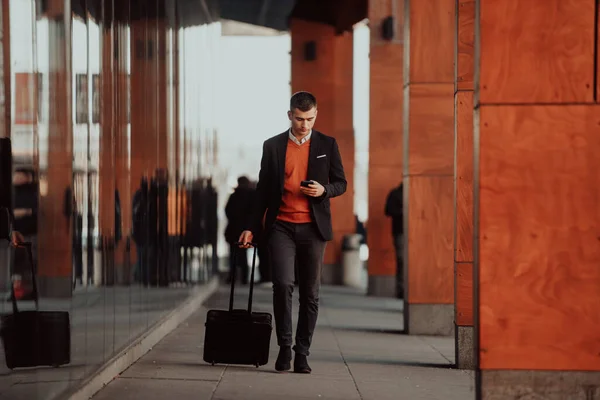 Je vais à l'aérogare. Homme d'affaires confiant voyageur marchant dans les rues de la ville et tirant sa valise boire du café et parler sur smartphone — Photo