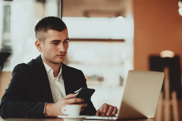 Homem de negócios feliz sentado na cafetaria com laptop e smartphone — Fotografia de Stock